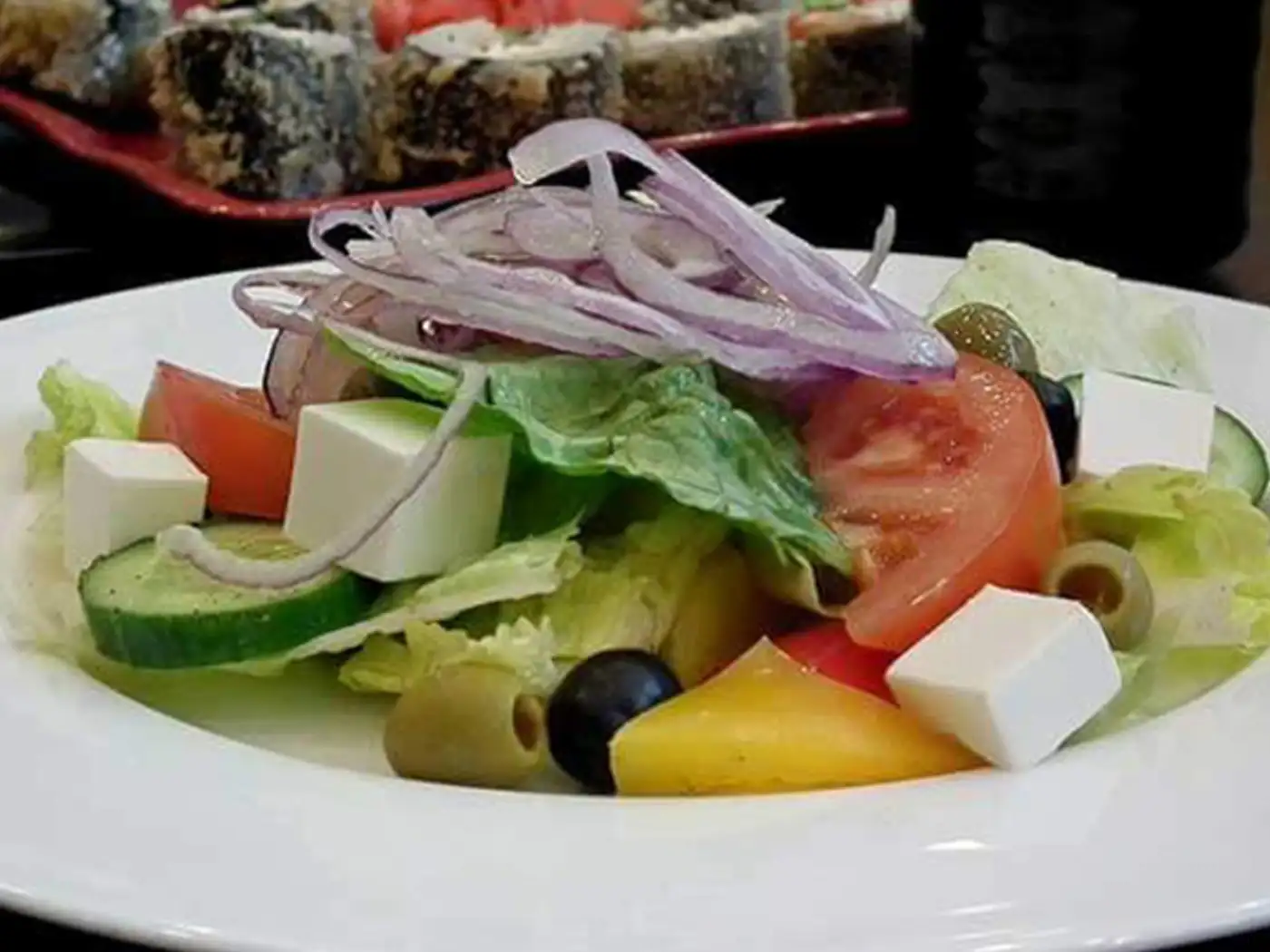 Greek salad with feta, tomatoes, cucumbers, olives, and red onion on a white plate.