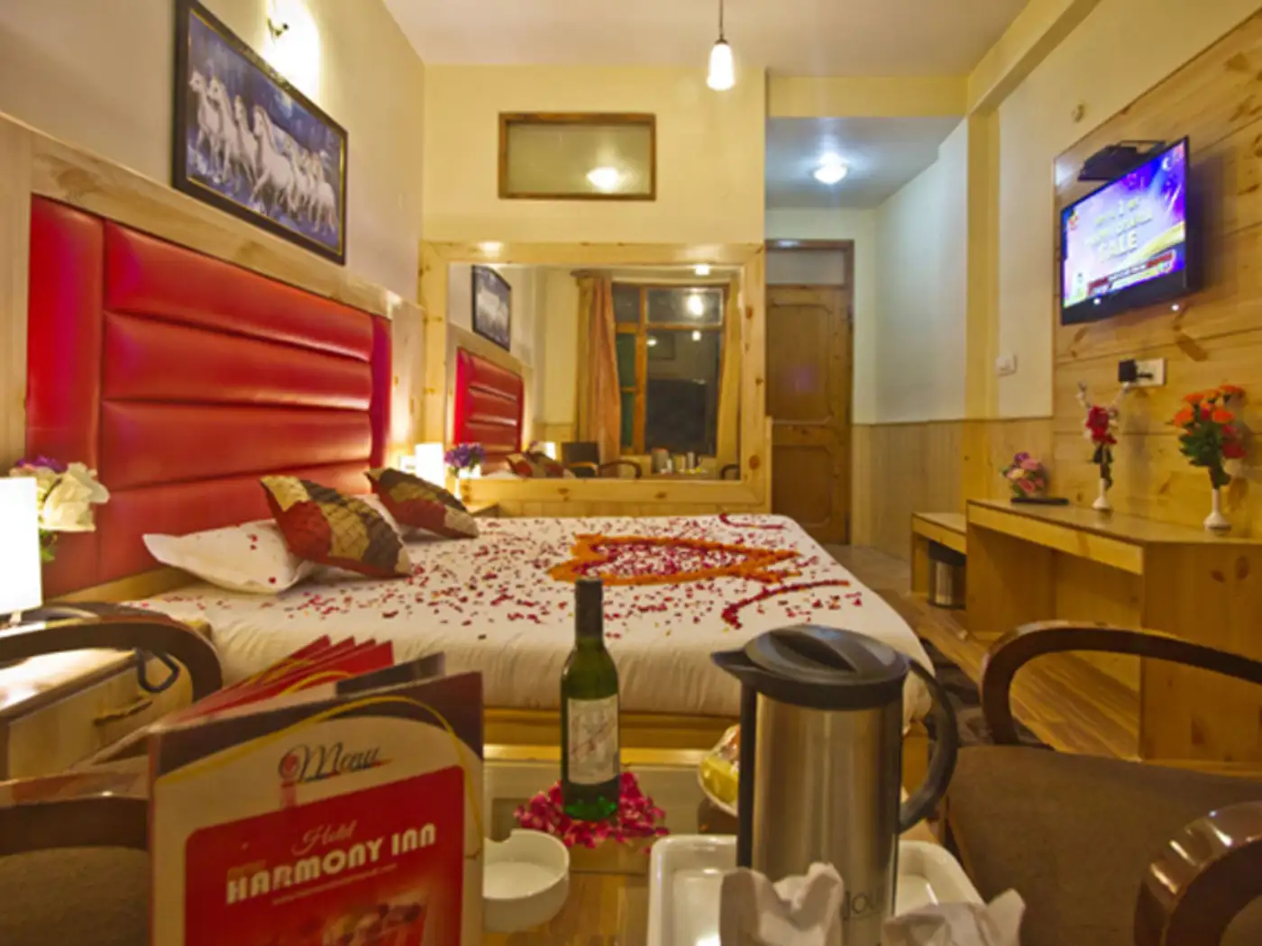 Romantic hotel room with rose petals on bed, wine, and menu