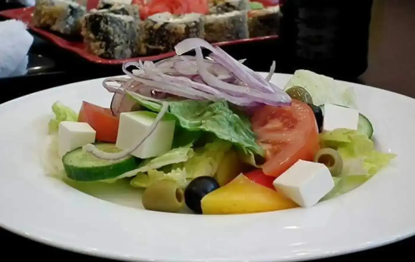 Greek salad with feta, tomatoes, cucumbers, olives, and red onion on a white plate.