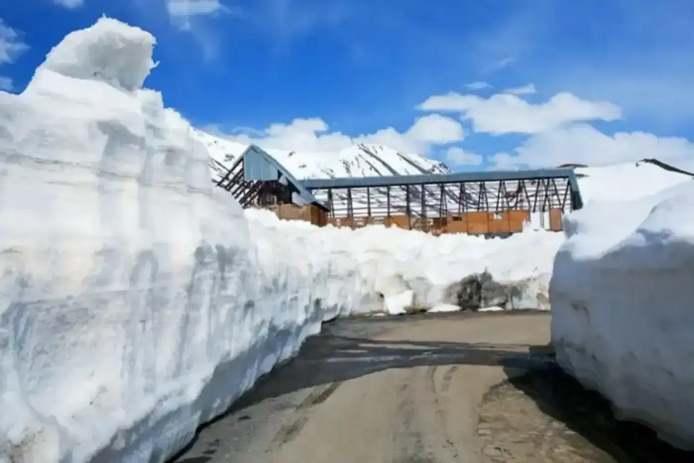 Road cut through deep snowdrifts with a building in the background.